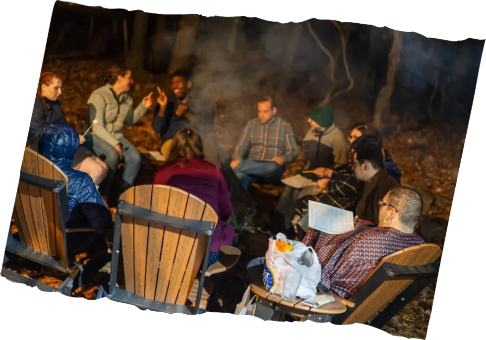 Players gathered around a campfire in the woods, a game in progress.