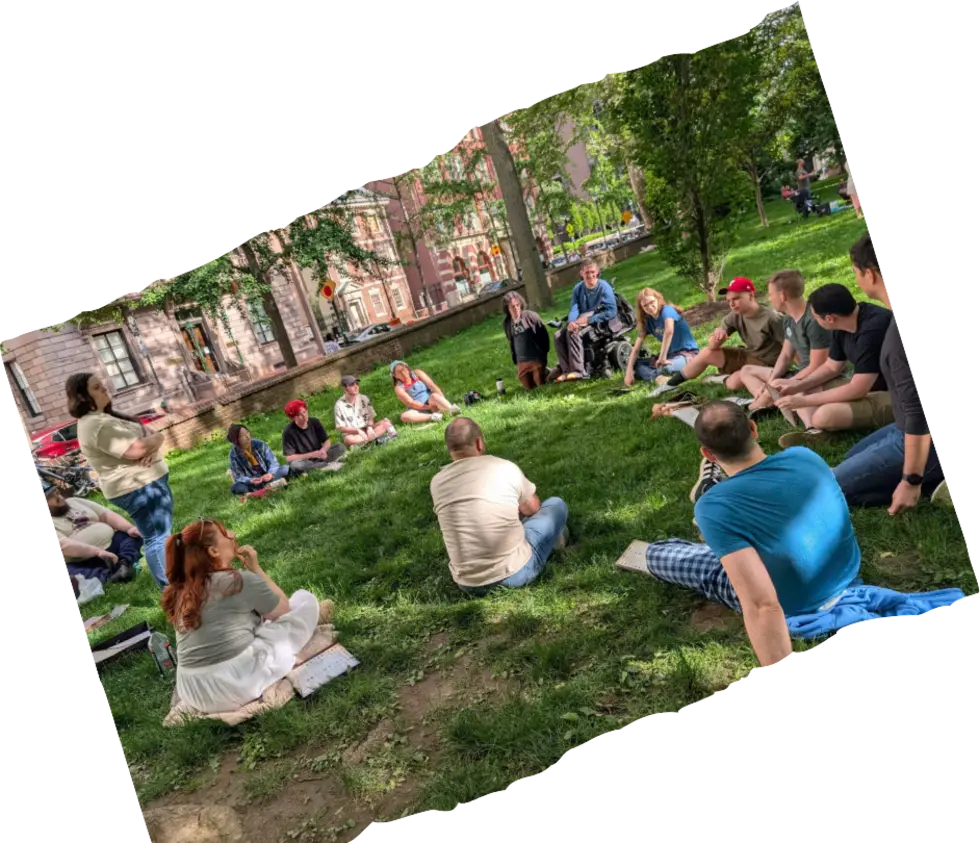A large circle of players sitting on a park lawn in the sun.